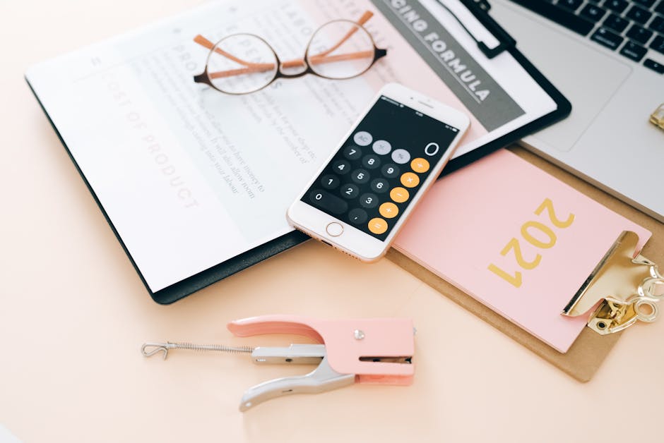 An elegant flat lay of stylish office supplies, including a calculator on a smartphone, stapler, and clipboard.
