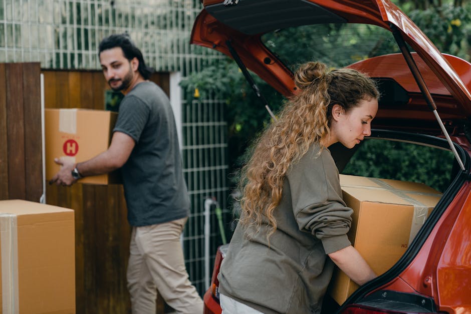 Young diverse couple in light casual clothes unloading boxes of stuff from automobile in green garden of newly purchased home